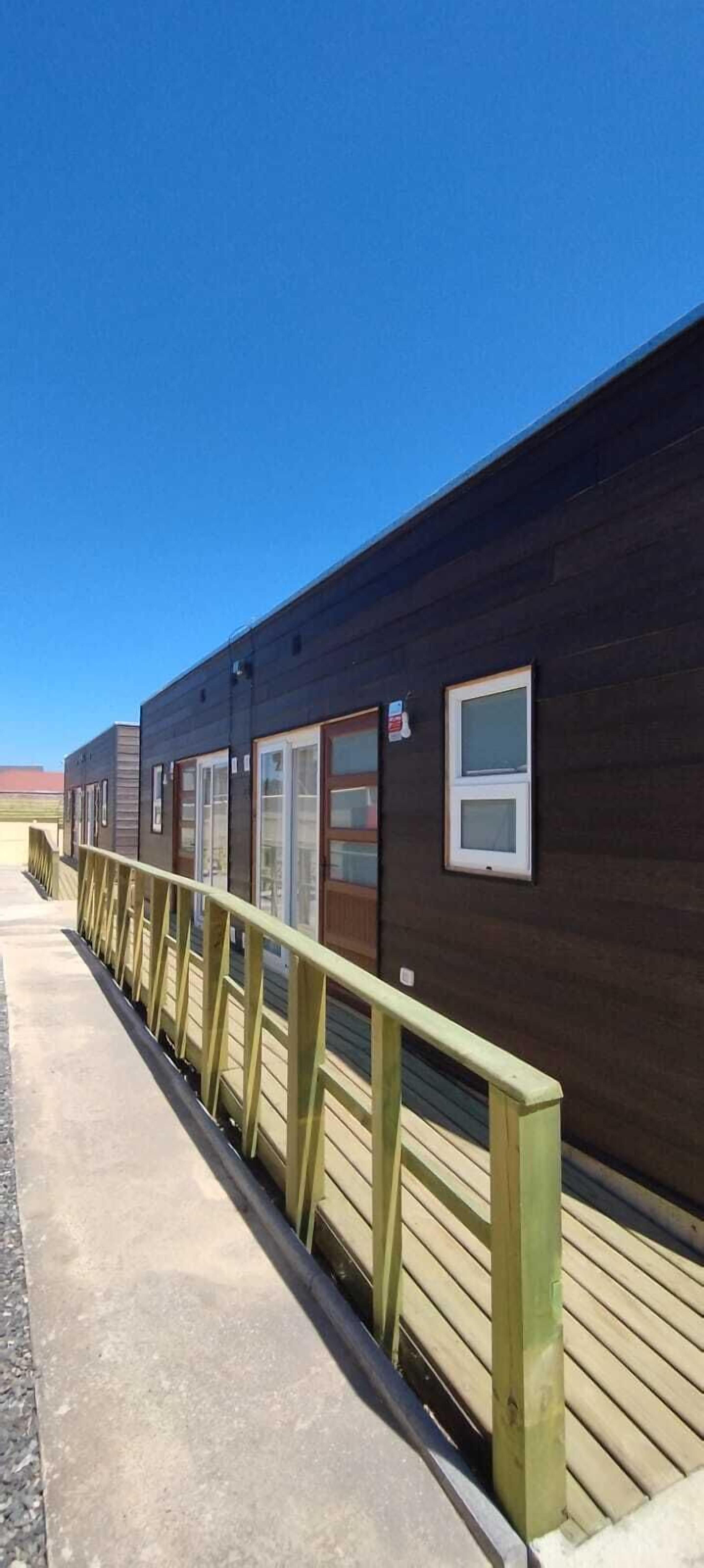 A row of dark wooden cabins with windows and a wooden deck in front.