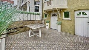 Un patio con un banco de madera, baldosas con diseños y una puerta blanca.