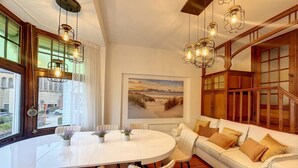 Una sala de estar moderna con una mesa de comedor redonda blanca, sofás color beige y un amplio ventanal con cortinas.