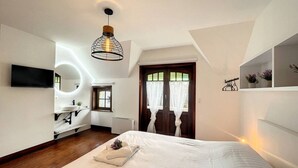 Un dormitorio moderno con una cama grande, un televisor montado en la pared, una mesita de noche con una planta y una ventana con cortinas.