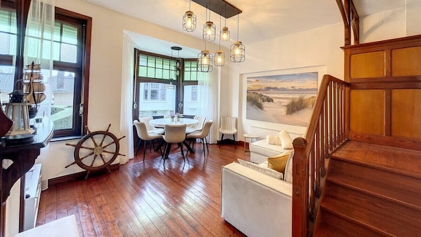 Amplia sala de estar con escalera de madera, mesa de comedor con sillas y un ventanal con vistas.