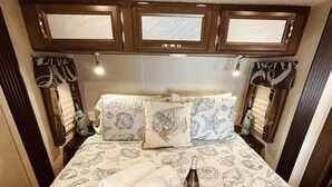 A bed with a seashell patterned bedspread, two pillows, a bottle of champagne, and two rolled towels. - Book now! Special prices for the holidays and 2026 rentals! (Key Largo)