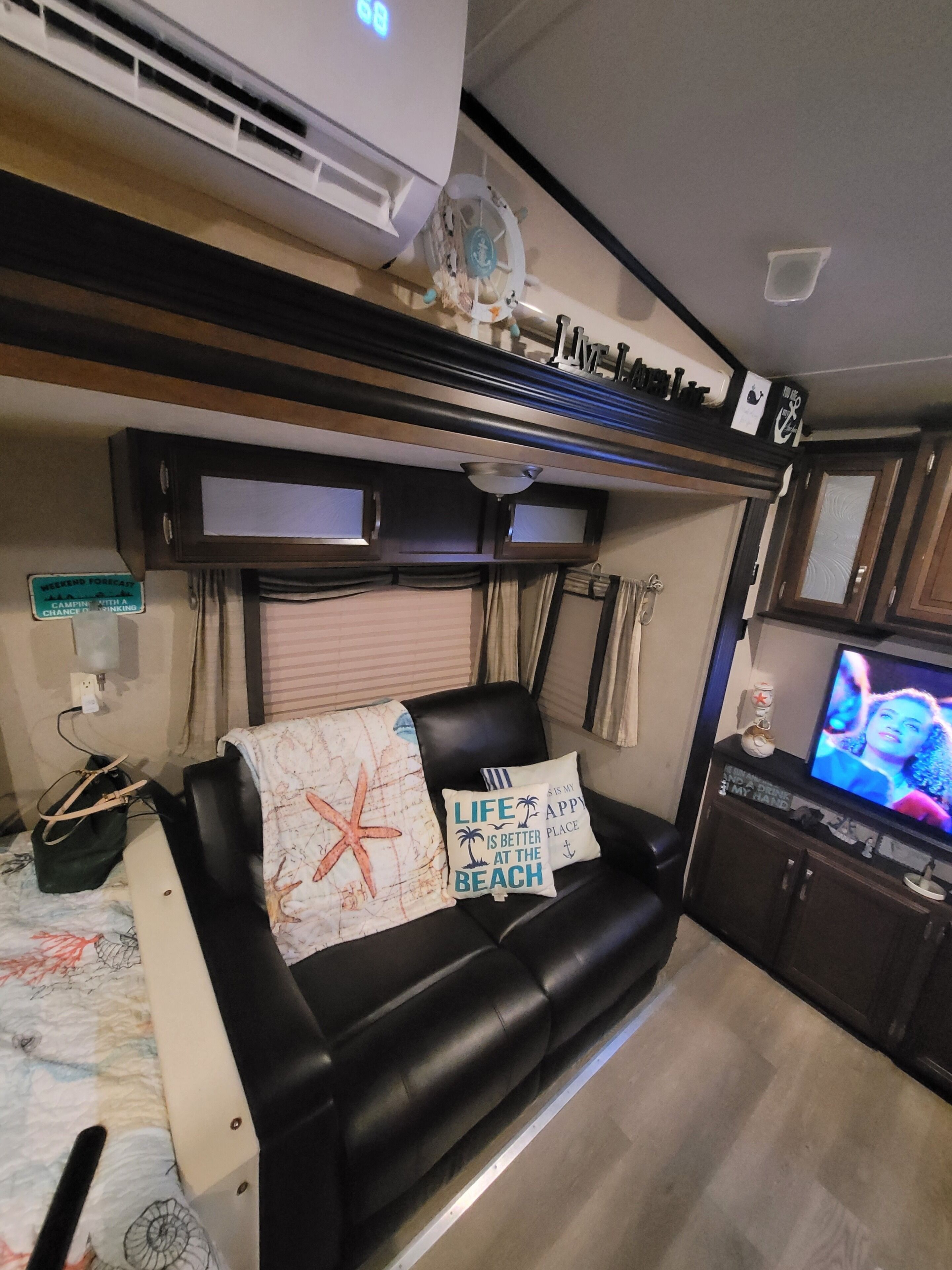 A compact living space with a black leather sofa, a television, and a small kitchenette area.
