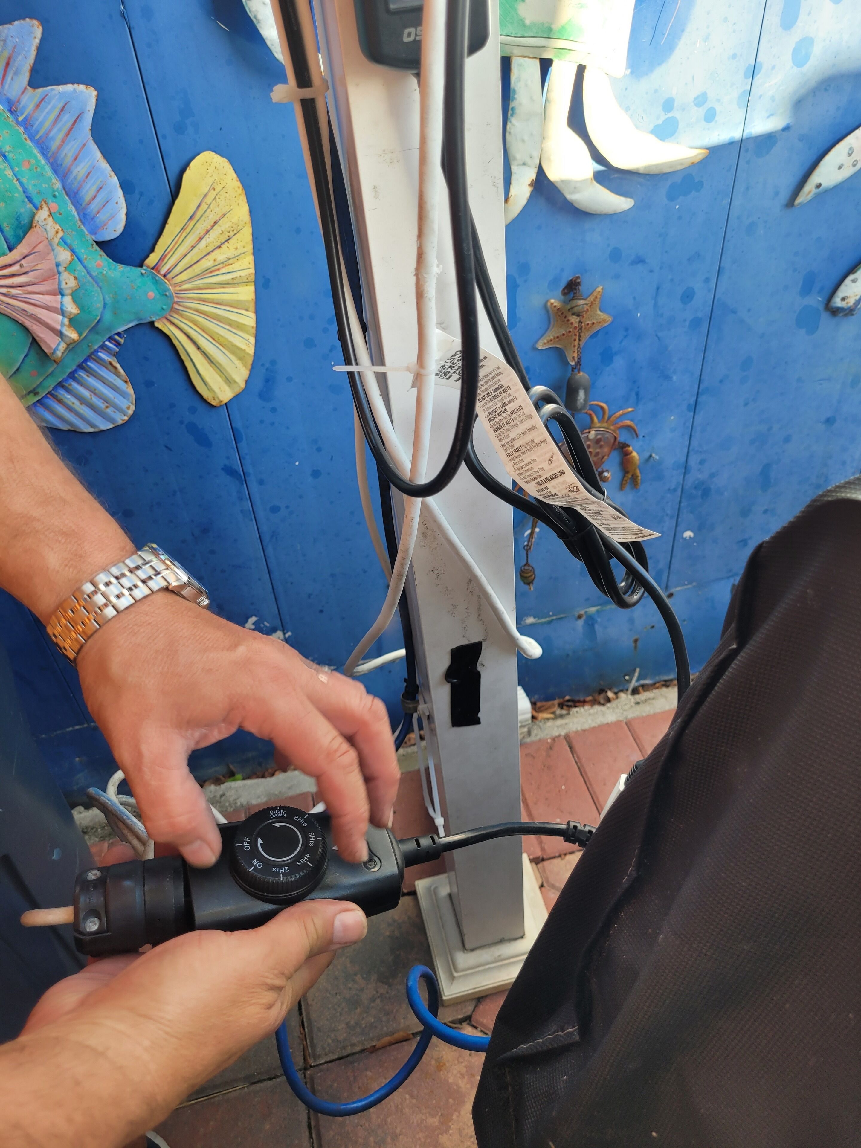 A person adjusting a device with a cable connected to a blue wall with decorative fish and a star ornament.