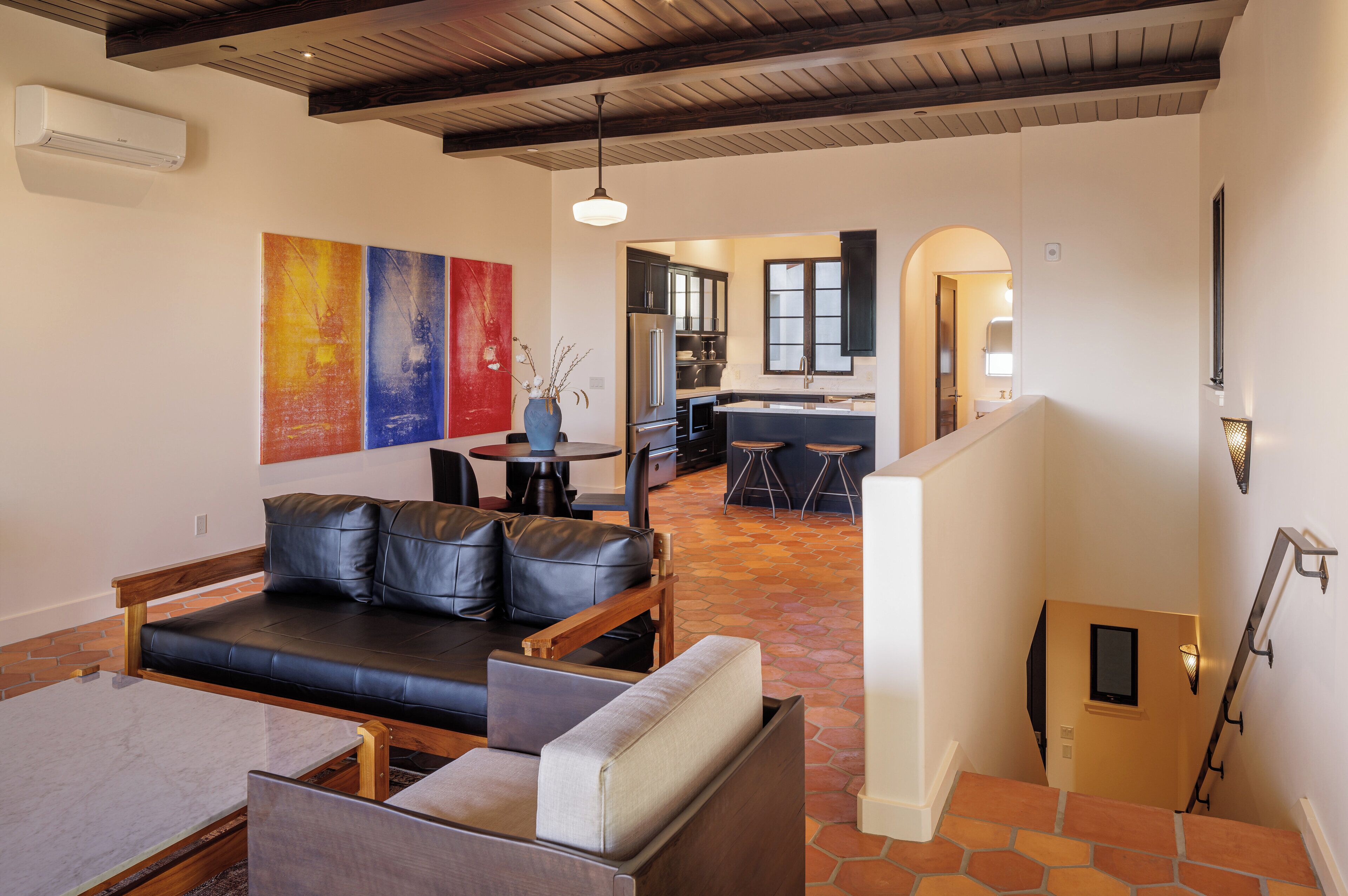 Un intérieur moderne avec un canapé en cuir noir, une table à manger et un coin cuisine doté de meubles sombres et d’un réfrigérateur en acier inoxydable.