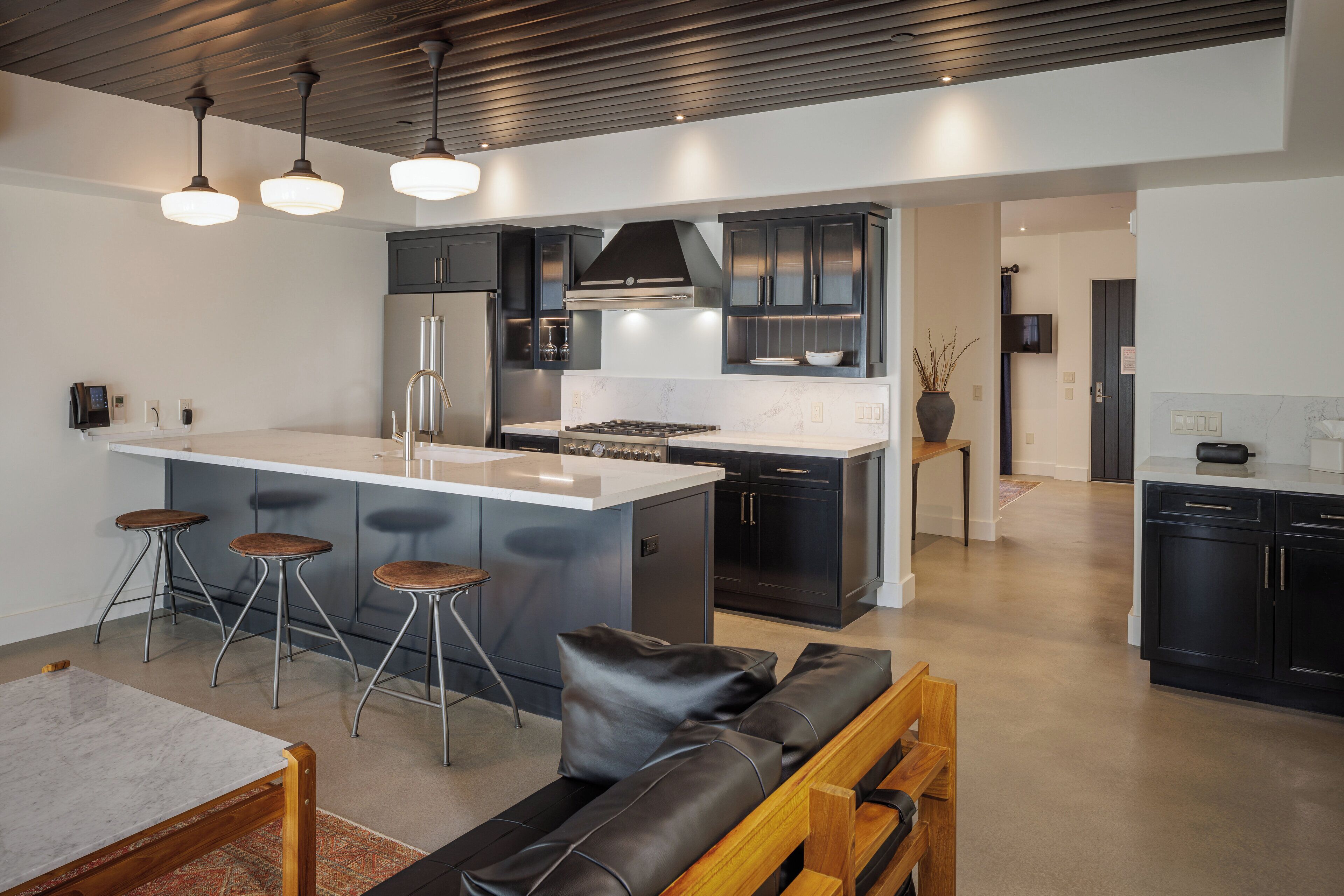 Cocina moderna con una isla central, taburetes de bar, un banco de madera y un televisor al fondo.