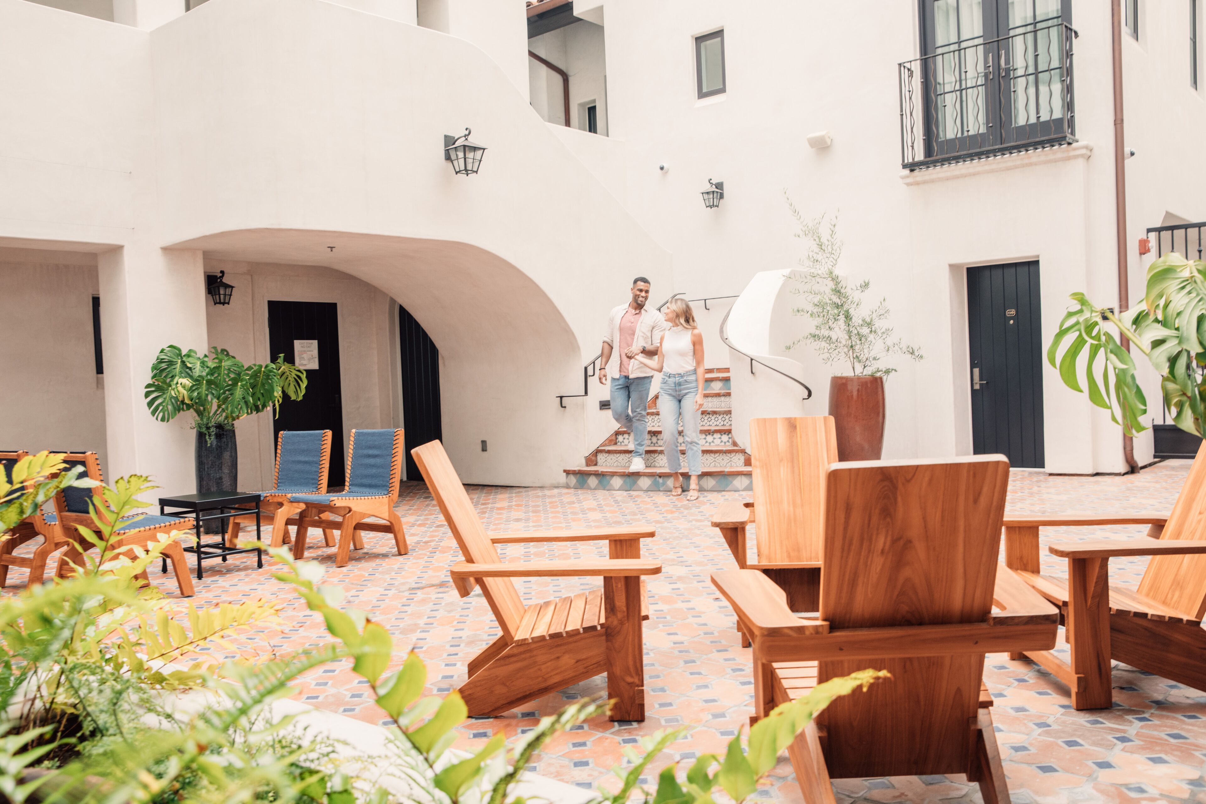 A courtyard with wooden chairs and tables, a staircase, and potted plants.