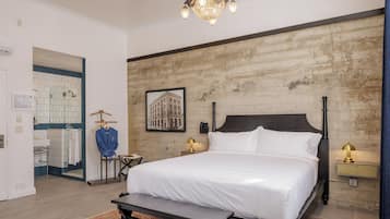 Hotelkamer met een groot bed, een kroonluchter, een ingelijst schilderij aan de muur en een badkamer die door een geopende deur zichtbaar is.