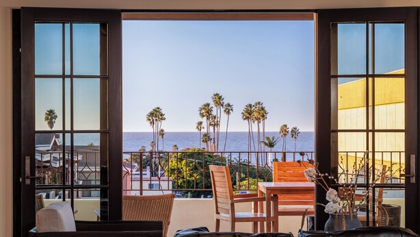 Een balkon met uitzicht op de oceaan en palmbomen, ingericht met een bank, stoelen en een tafel.