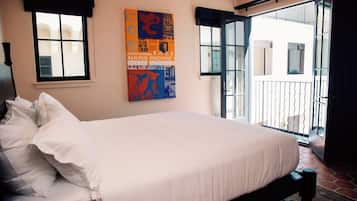 A neatly made bed with white linens, a large window with a black valance, and a colorful poster on the wall.