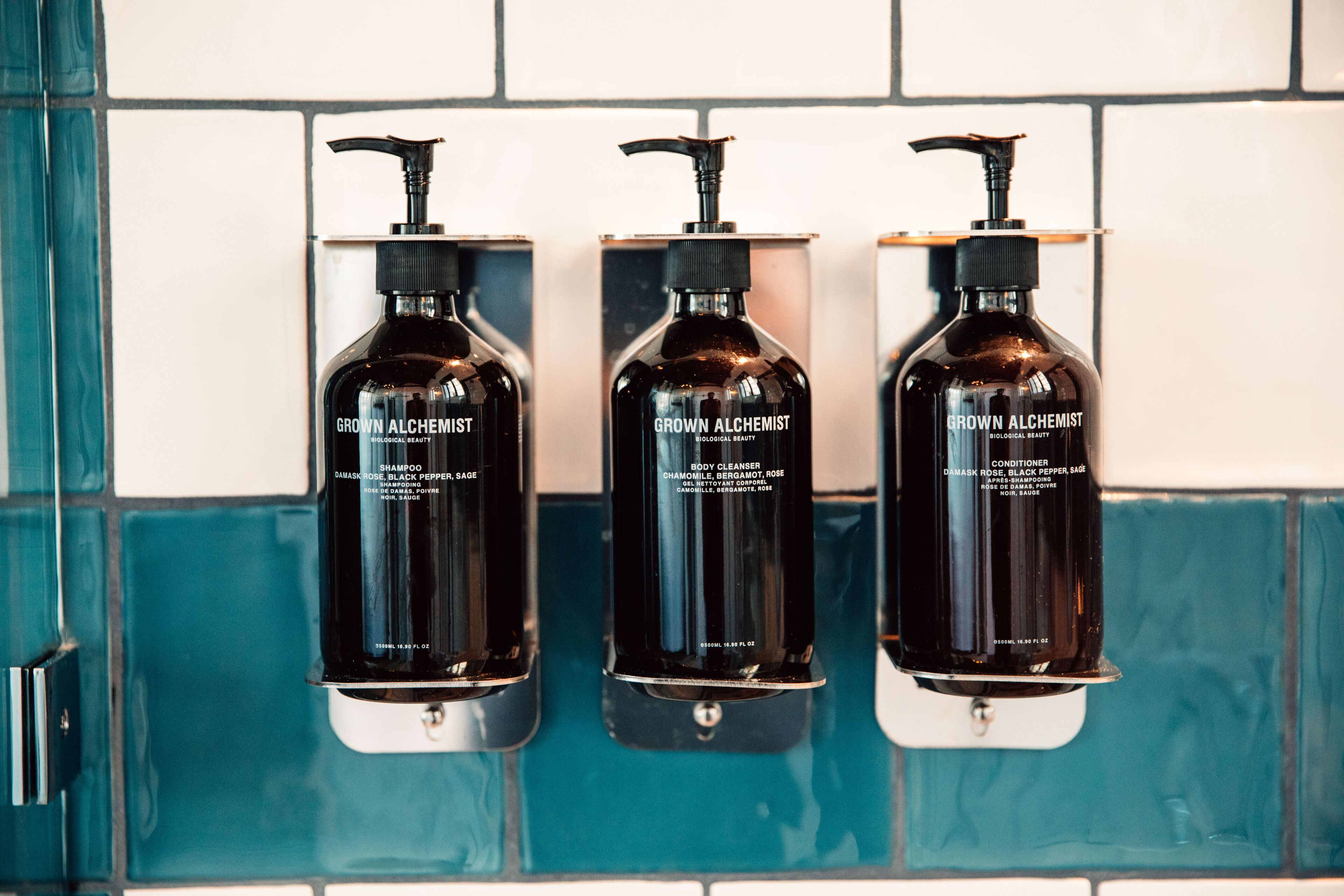 Tre sorte flasker med 'Grown Alchemist' produkter hænger på en flisebeklædt væg.