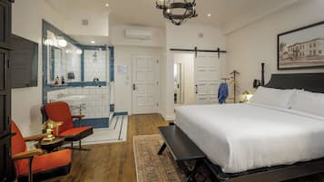 A hotel room with a large bed, a desk, a chair, a mirror, a chandelier, and a painting on the wall.