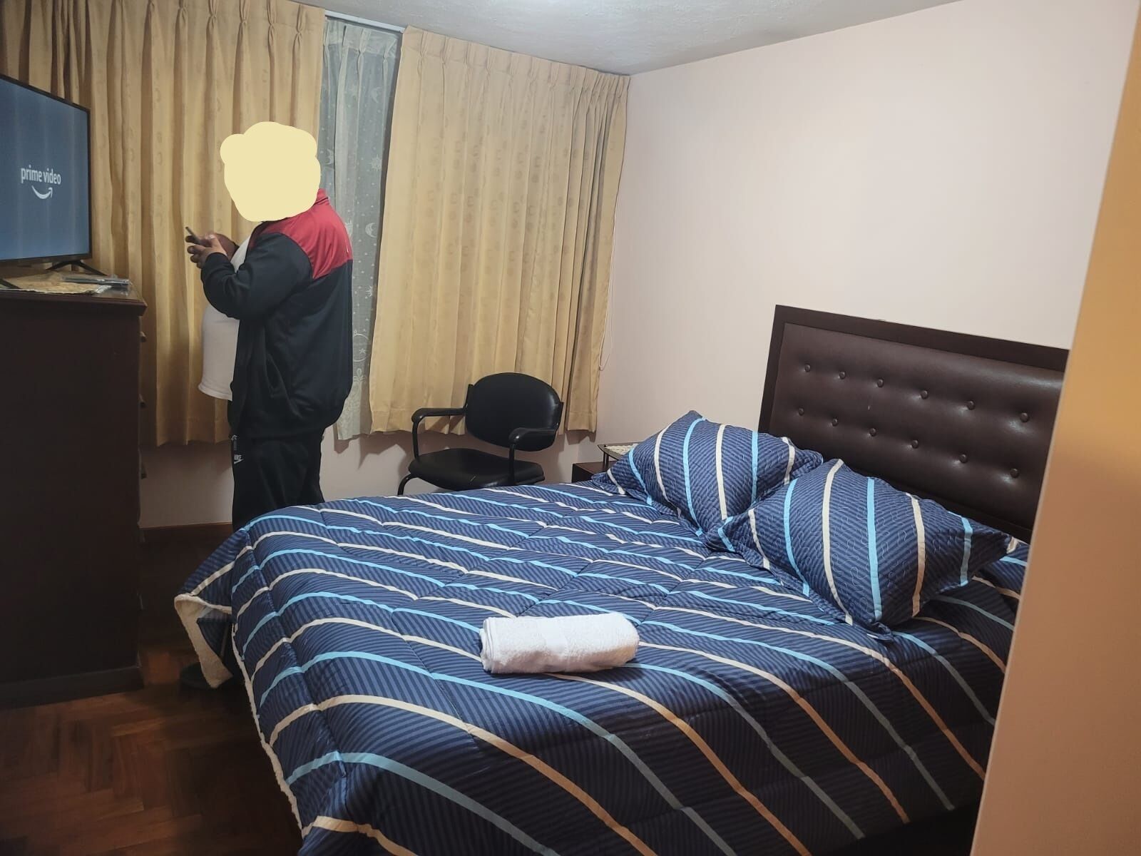 Habitación de hotel con cama, una silla, un escritorio con computadora y un televisor mostrando el logotipo de Prime Video.