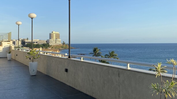 Una terraza en la azotea con plantas en macetas, barandilla y vista al océano.
