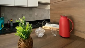 Una cocina con armarios blancos, encimera de madera, hervidor rojo, frasco de vidrio y planta en maceta.