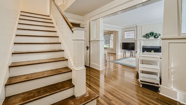 A staircase with wooden steps and white railings leading to a room with a fireplace, a TV, and a white cart. - Prime Location walk to attractions w Free Parking (Seattle)