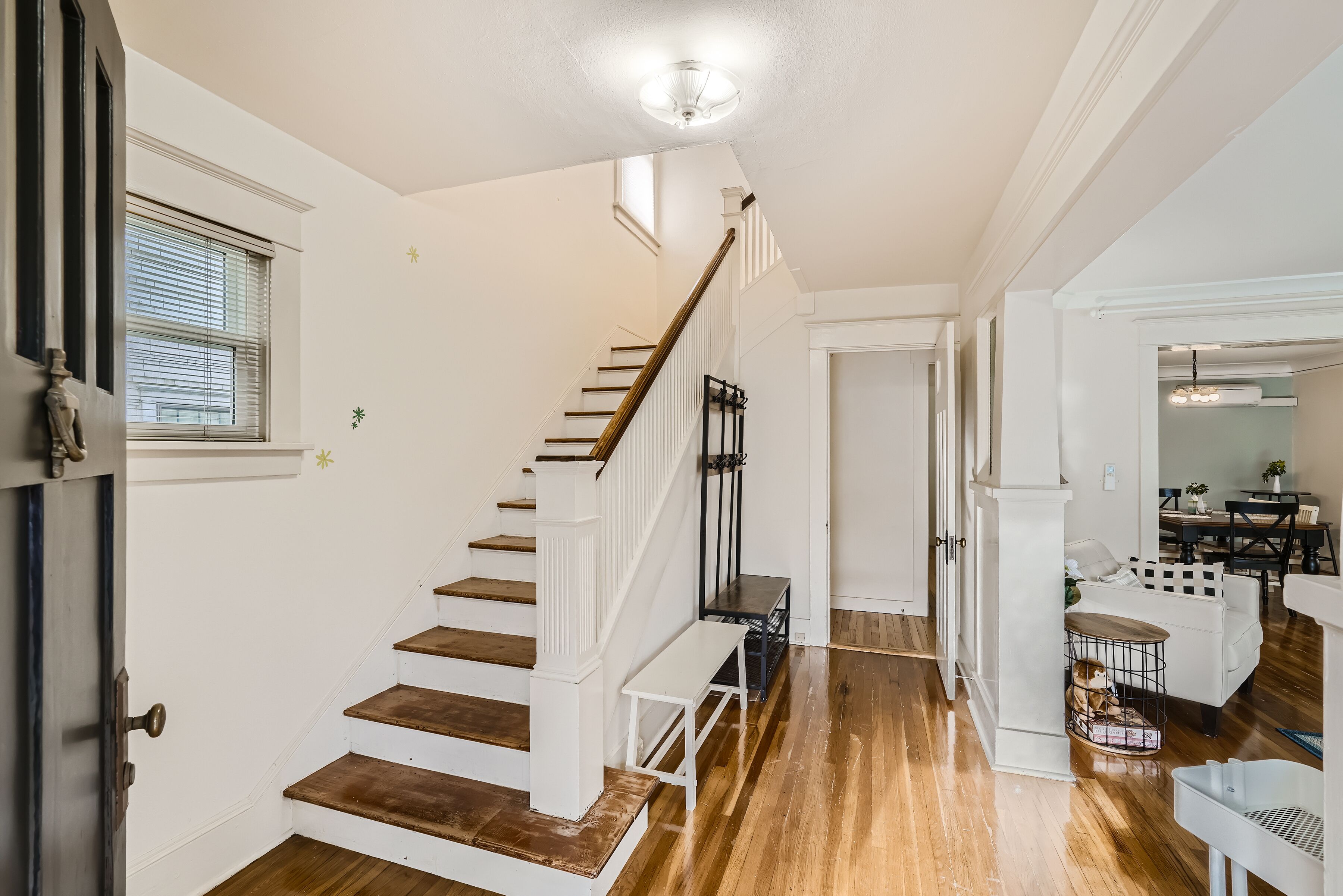 A staircase with wooden steps and white railings, leading to a room with a dining area and a pet cage.
