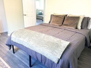 A bedroom with a large bed, a bedside table, and a door leading to another room. - Western Homefront (Vista Creek Pt)