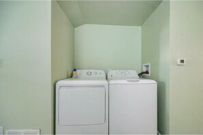 A laundry room with two stacked washers and dryers, a power outlet on the wall, and a thermostat on the wall.