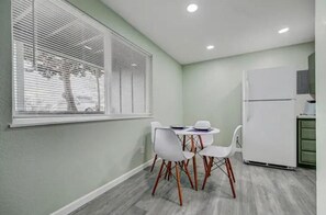A small kitchen with a white refrigerator, a dining table with four chairs, and a window with blinds. - Western Homefront (Vista Creek Pt)