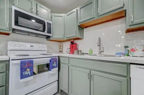 A kitchen with light green cabinets, a white stove, and a microwave. - Western Homefront (Vista Creek Pt)