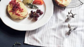 A plate with two open-faced sandwiches topped with cheese and red onions, accompanied by pickles, a slice of tomato, and grapes.