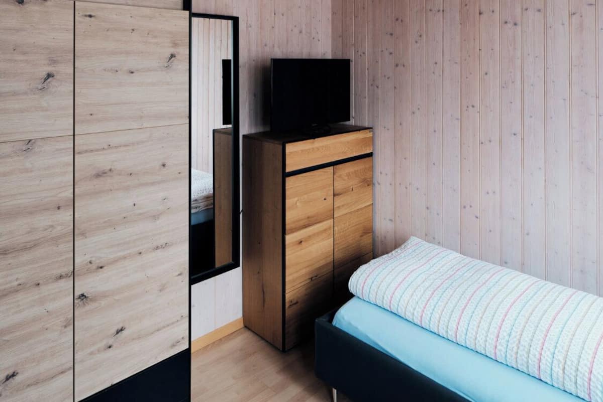 Un dormitorio con cama, cómoda, televisor encima de la cómoda y espejo en la pared.