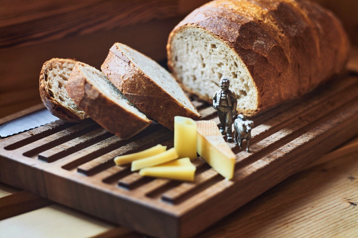 Une miche de pain sur une planche à découper en bois, accompagnée de fromage et d’une figurine.