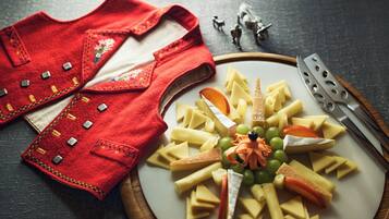 A plate of assorted cheeses and fruits on a wooden board, accompanied by a red garment with decorative stitching.