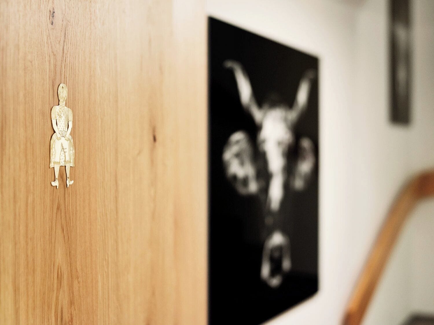 A wooden door with a small cut-out figure, a black and white photograph on the wall, and a partial view of a chair.