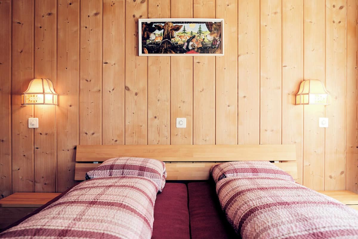 Una habitación con paredes de madera, una cama con dos almohadas y dos lámparas fijadas a la pared.