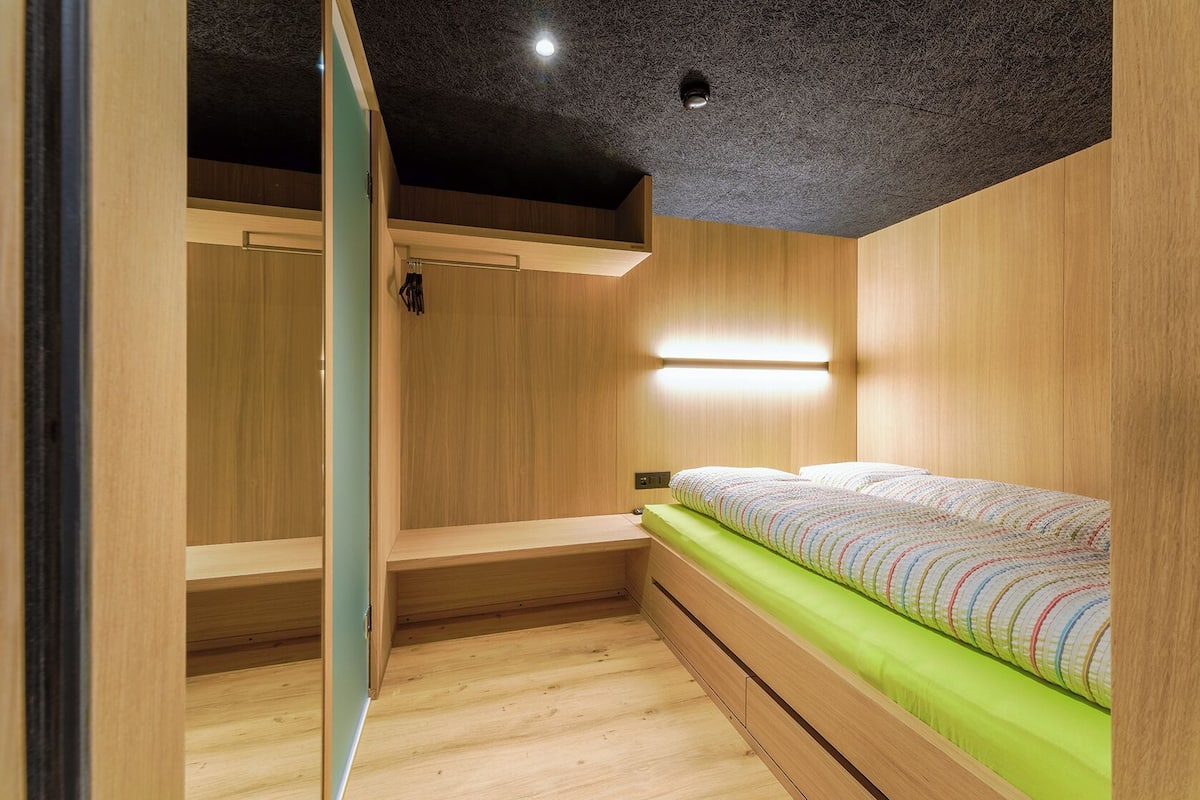 Un dormitorio pequeño con una cama litera, paredes de madera, colchón verde y una lámpara en el techo.