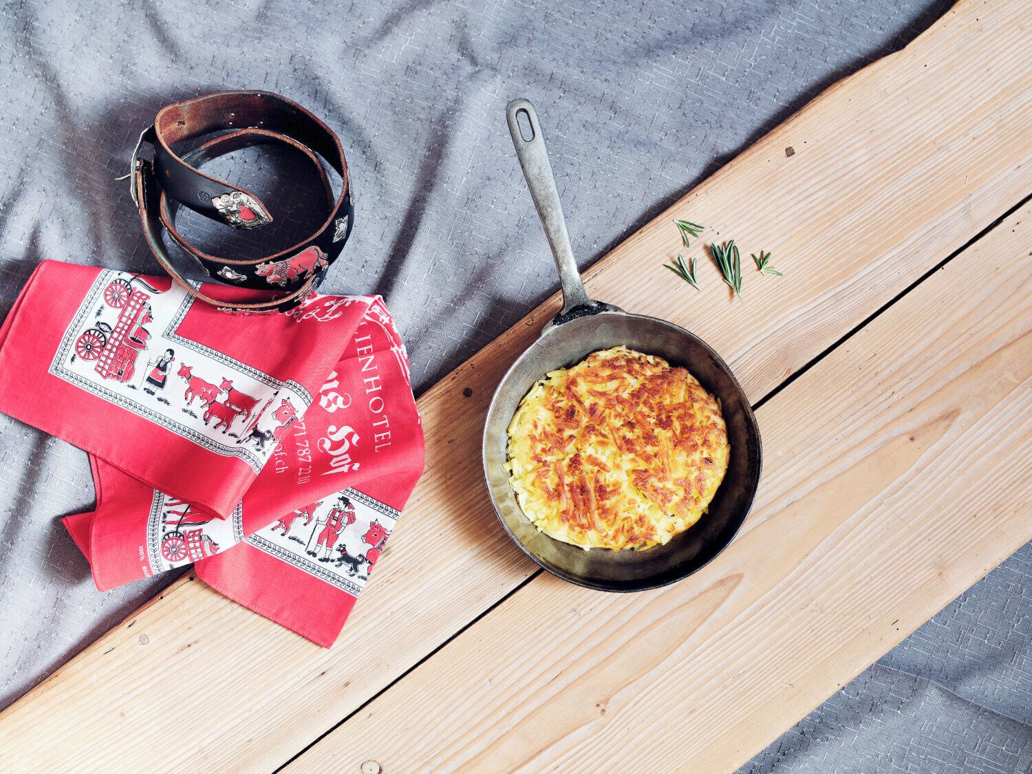 A skillet with a dish on a wooden board, a red cloth with a horse pattern, and a metal belt.