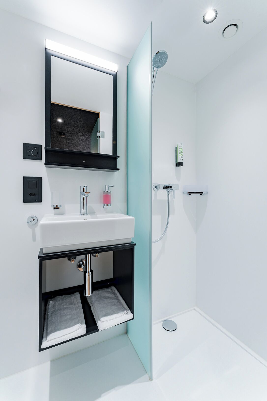 A modern bathroom with a white sink, a mirror, and a shower.