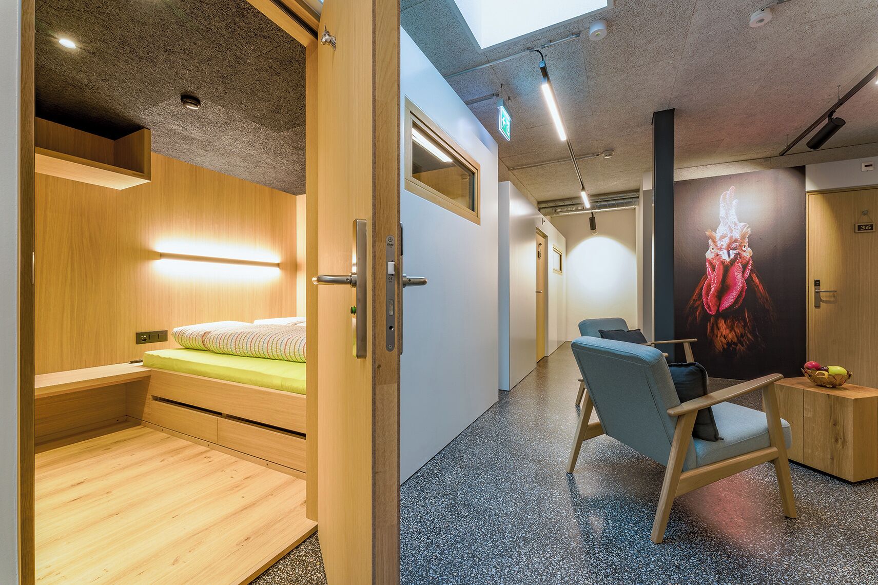 Camera d'albergo moderna con un letto in legno, una scrivania, una sedia e un grande quadro di un gallo appeso al muro.