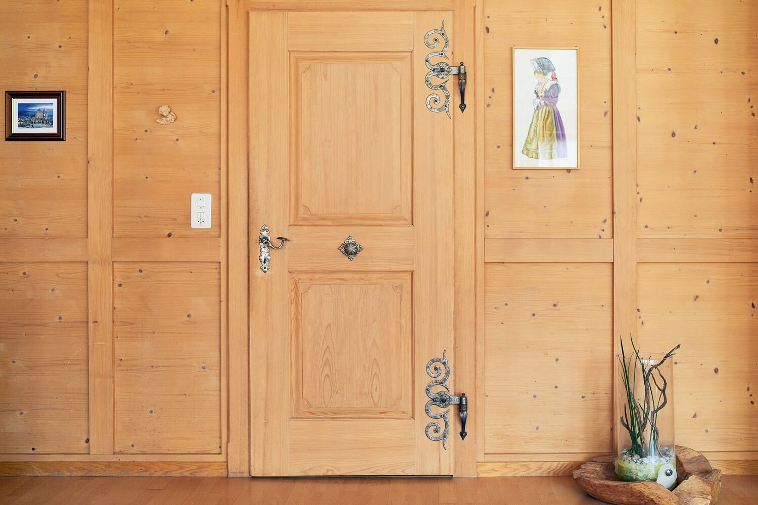 Une porte en bois ornée de poignées métalliques décoratives et d’une petite plaque ornementale.