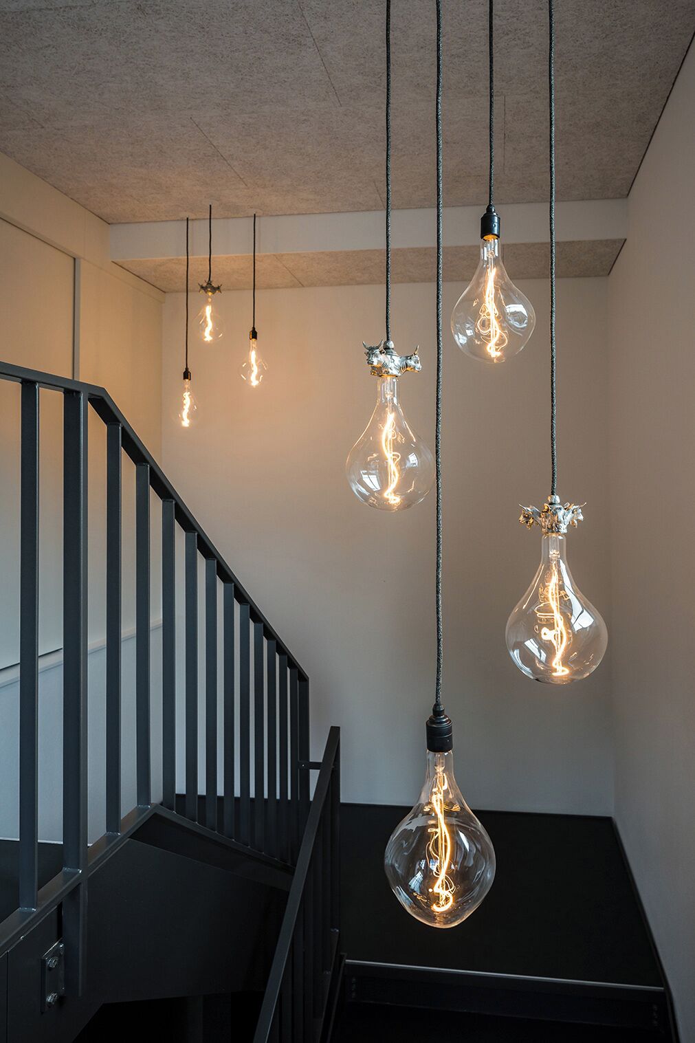 A staircase with a black railing and hanging light bulbs with a unique design.
