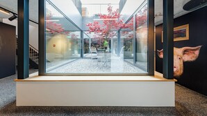 A modern interior with a glass enclosure displaying a courtyard with red foliage and seating. - Gasthaus Hof (Appenzell)