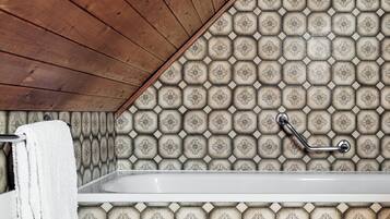 Un baño con techo de madera, una bañera y pared de azulejos estampados.