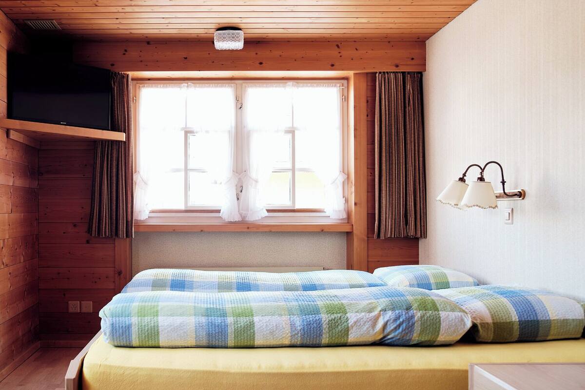 Una habitación acogedora de madera con una cama, una ventana con cortinas y una lámpara fijada a la pared.