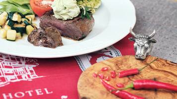 Un plato con bistec, verduras y una cucharada de salsa, una figurita de toro y chiles sobre una tabla de madera.
