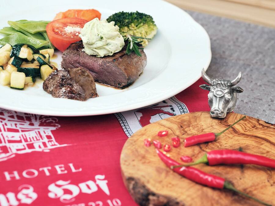 Un plato con bistec, verduras y una cucharada de salsa, una figurita de toro y chiles sobre una tabla de madera.