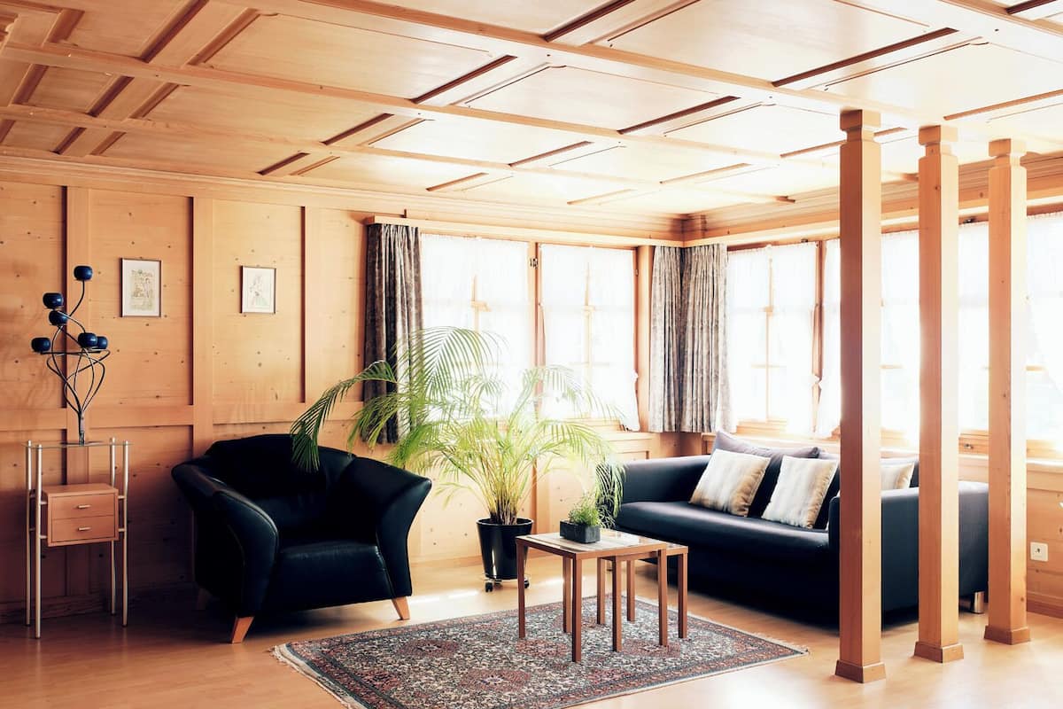 Una sala de estar moderna con paneles de madera, un sofá de cuero negro, un sillón negro, una mesita de madera y una planta en maceta.