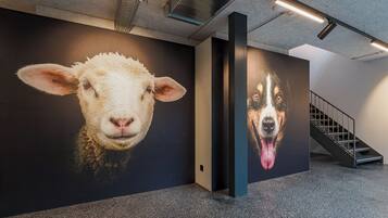 A hallway with a large wall mural of a sheep and a dog, a staircase, and a ceiling with exposed beams and lighting fixtures.