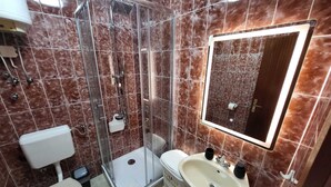 A bathroom with a glass-enclosed shower, a toilet, a sink with a mirror, and marble-tiled walls. - KABLAR'S SUNNY SUITES 1BR APT with balcony and sea view (Dubrovnik)