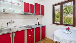 A kitchen with red cabinets, a stainless steel sink, and a window with a view of greenery. - KABLAR'S SUNNY SUITES 1BR APT with balcony and sea view (Dubrovnik)