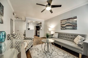A modern living room with a grey sofa, patterned armchairs, a glass coffee table, and a ceiling fan. - I28 - Apt|Patio|10mi to Convention Ctr|Sleeps 2 (Irving)