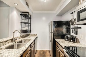 A compact kitchen with a granite countertop, stainless steel appliances, and a black refrigerator. - I28 - Apt|Patio|10mi to Convention Ctr|Sleeps 2 (Irving)