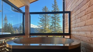 Una cabaña de madera con un ventanal grande que ofrece vistas a montañas nevadas y árboles.