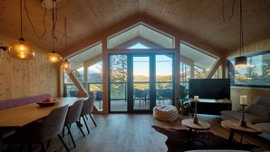 Un loft espacioso con techo alto, un comedor con mesa y sillas de madera, una zona de estar acogedora con sofá y televisor, y ventanas grandes que ofrecen vistas al exterior.